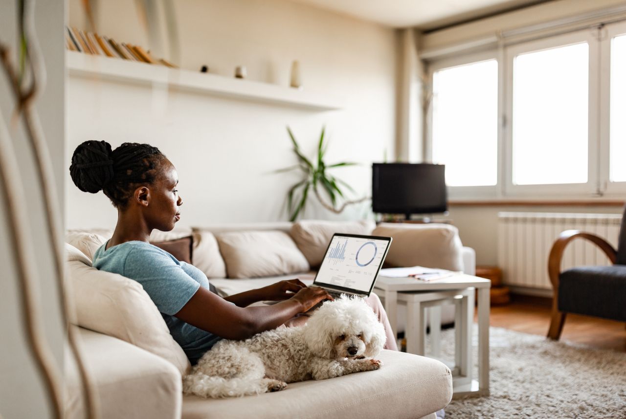 woman sitting on couch working on computer with dog next to her
